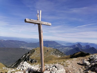 Croix sommitale symbolisant la fin de l'ascension du Mont Colombier, avec le lac d'Annecy en arrière-plan